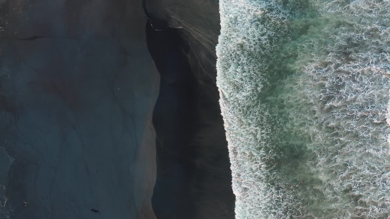 鸟瞰美丽的海滩，海浪和水从顶部角度撞击黑色的沙滩视频素材