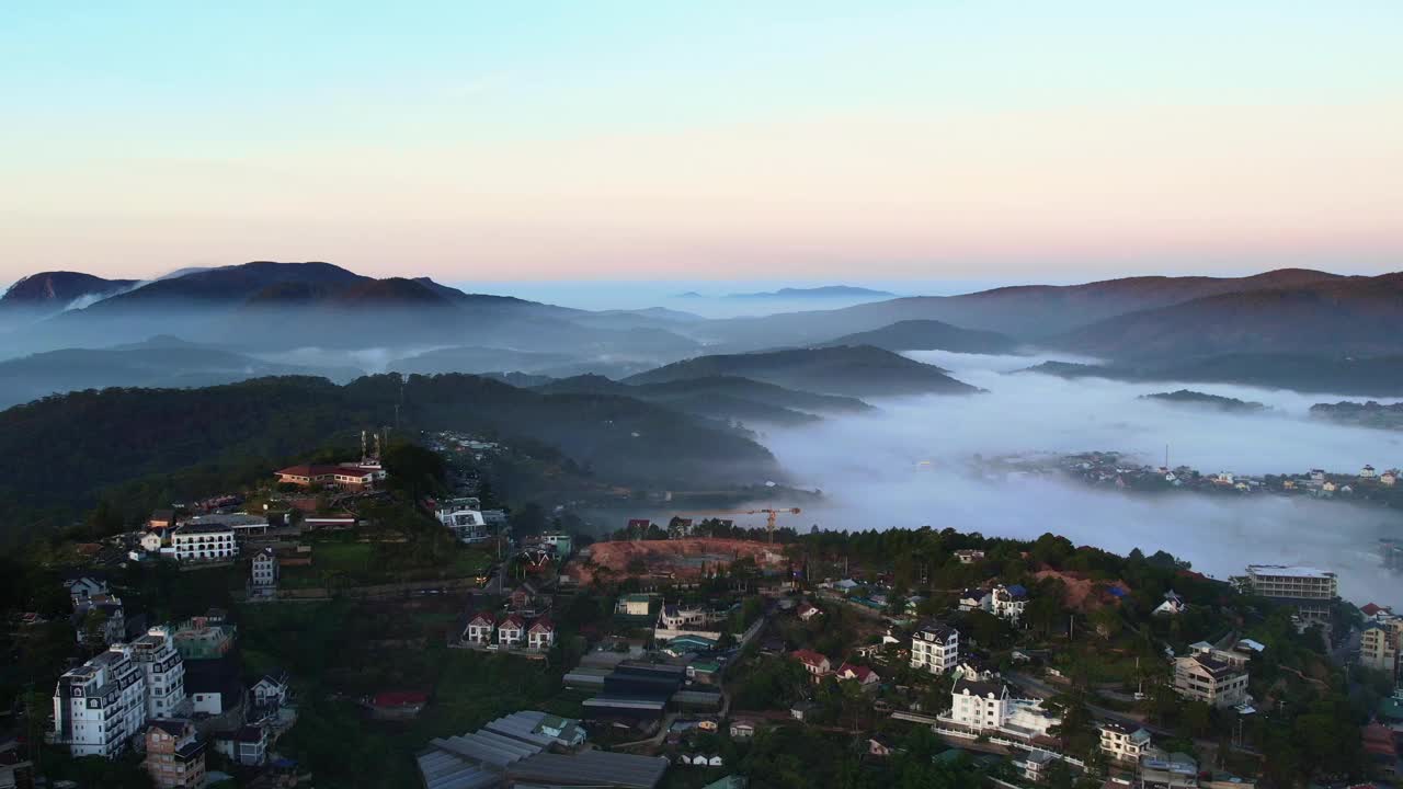 黎明时分大叻市的宁静景色，坐落在连绵起伏的群山中，雾气笼罩着景观，建筑物在雾中窥视，展示了自然的和谐融合视频下载