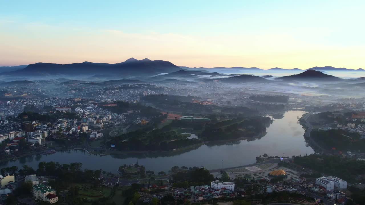 黎明时分，大叻市何宣香湖的宁静景色，周围是薄雾缭绕的风景，群山和柔软天空下苏醒的城市景观视频素材