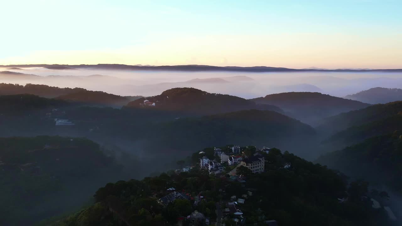 笼罩在薄雾中的达叻市宁静的景色，背景是山脉，上方是晴朗的天空，建筑物坐落在雾中出现的绿色植物中视频素材