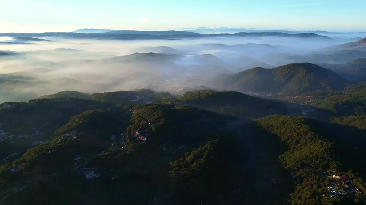 大叻市在雾山中的鸟瞰图，在晴朗的天空下，建筑坐落在郁郁葱葱的绿色植物之间，展示了一个宁静的景观。视频素材