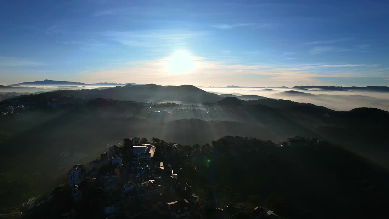 笼罩在薄雾中的达叻市令人叹为观止的景色，阳光透过云层投射出金色的光芒，照亮了坐落在郁郁葱葱的绿色植物和连绵起伏的山丘中的建筑物。视频素材