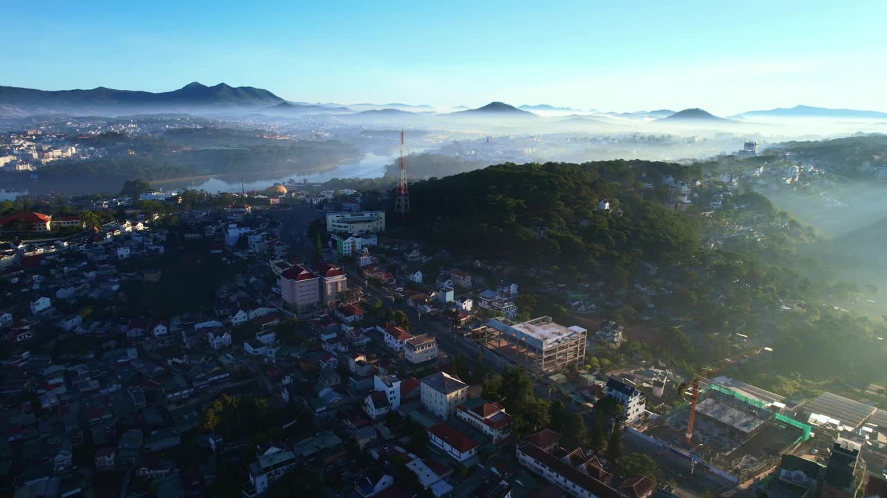 黎明时分的大叻市鸟瞰图，展示了城市地区，雾蒙蒙的山脉，以及郁郁葱葱的绿色植物中宁静的湖泊，在晴朗的天空下，创造了平静而风景如画的氛围。视频素材