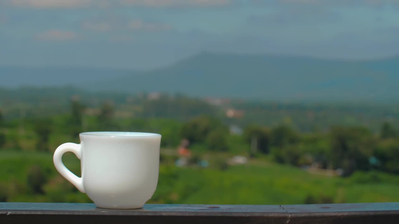 白色陶瓷咖啡杯放置在木制栏杆上，可以欣赏风景视频素材