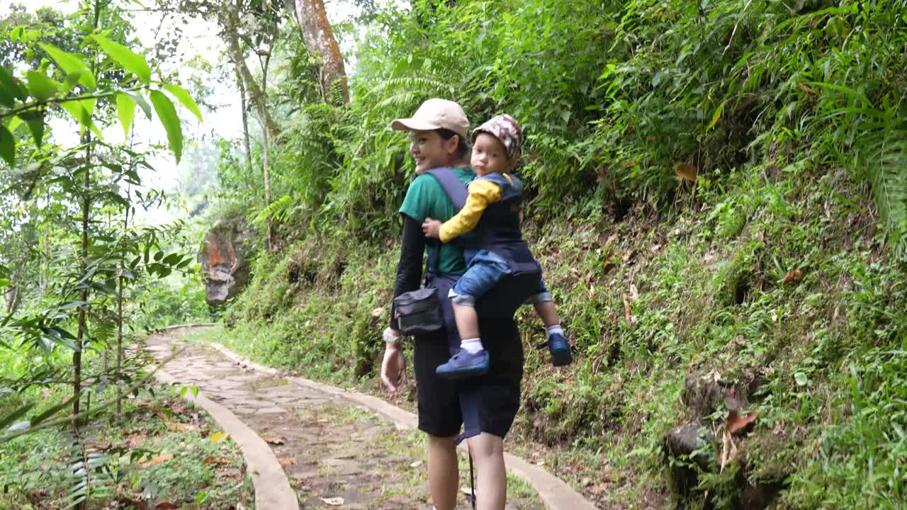 一位年轻的母亲背着孩子在森林里徒步旅行视频素材