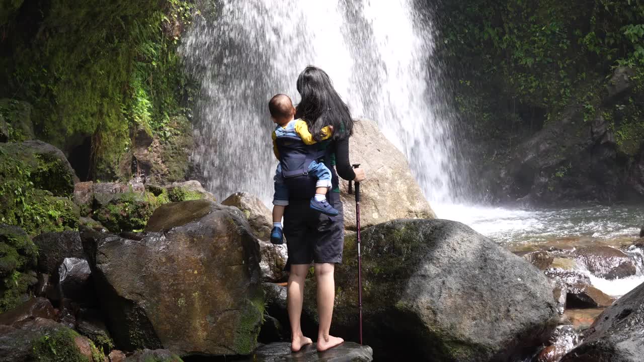 一位年轻的母亲背着孩子在森林里徒步旅行视频素材