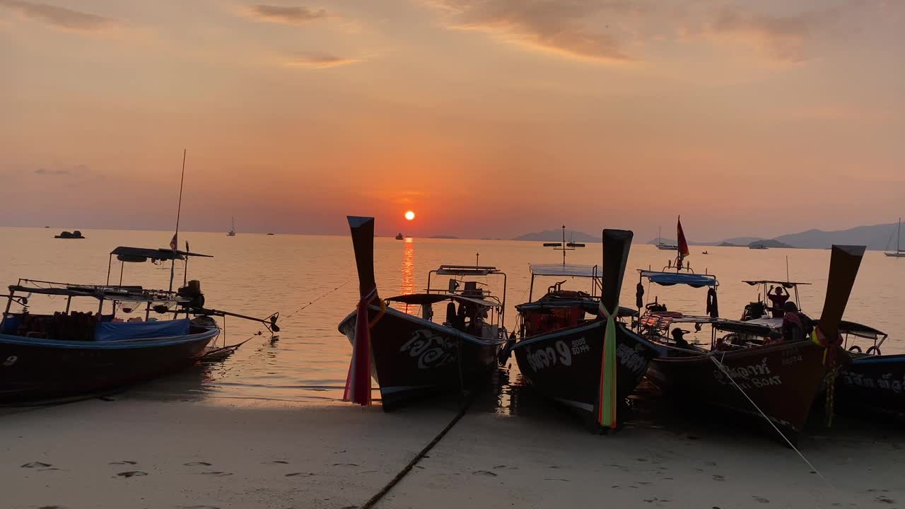 长尾船在沙滩上，夕阳和橙色的天空视频素材