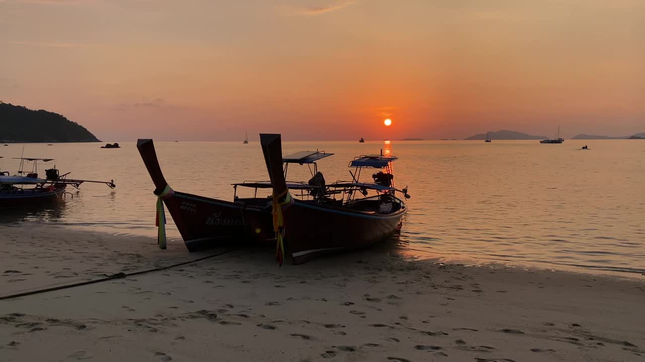 长尾船在沙滩上，夕阳和橙色的天空视频素材