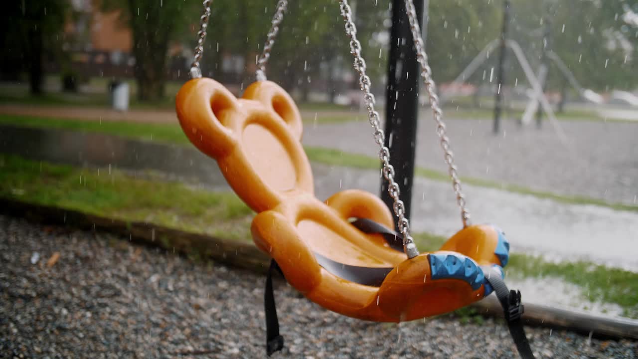 操场上的下雨天:孩子的秋千与雨滴和水坑的焦点视频素材