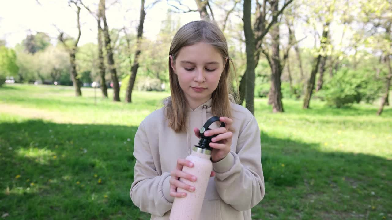 可爱的小女生在公园里从瓶子里喝水视频素材
