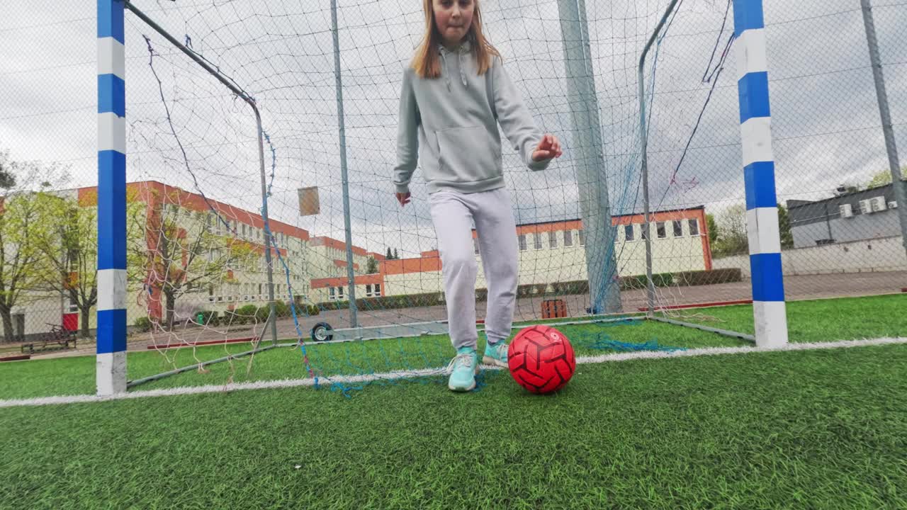 可爱的小女孩在绿色的足球场上用足球训练视频下载