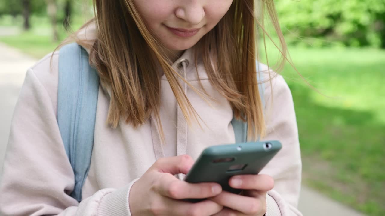 背着背包的小女孩在她的智能手机上输入短信视频素材