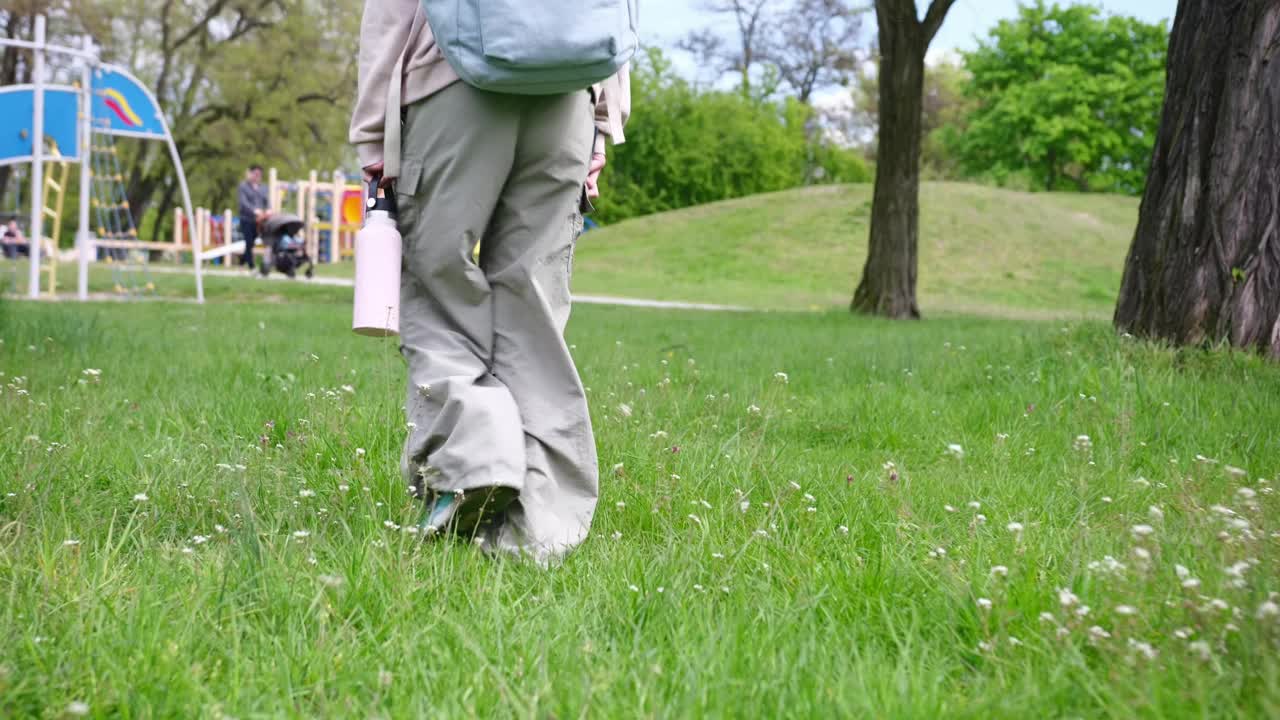 小女孩放学后在夏日公园散步，脚踩在草地上视频素材