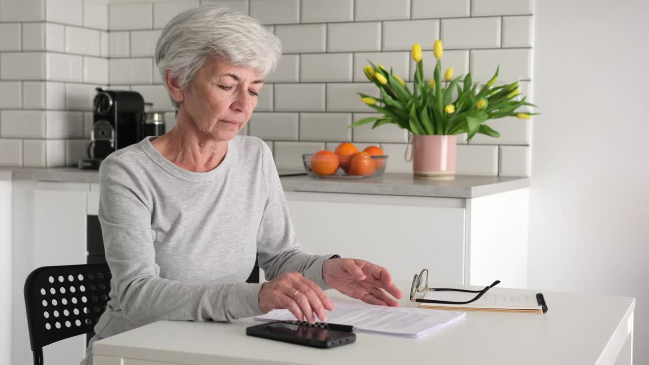 高级退休妇女在家里的厨房里检查合同中的数据视频下载