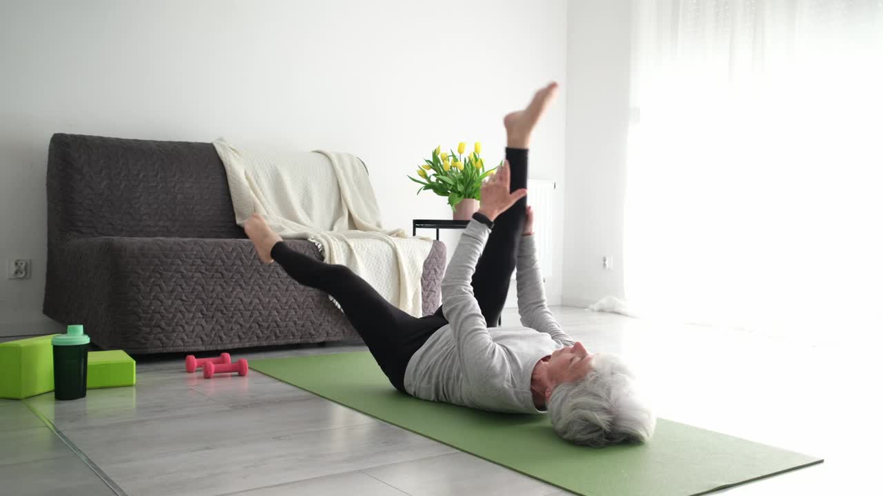 迷人的老年妇女在家里做瑜伽训练和伸展视频素材