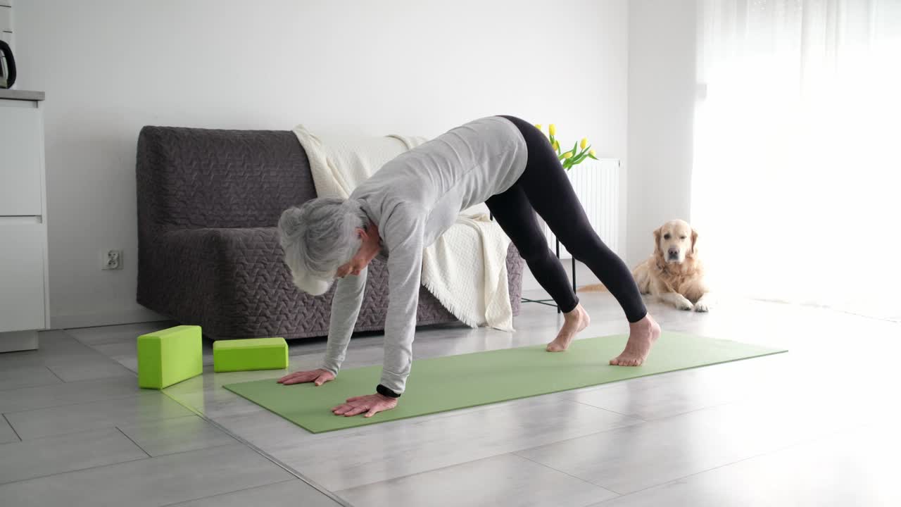 白发活跃的老年妇女在家里伸展瑜伽下犬式视频素材