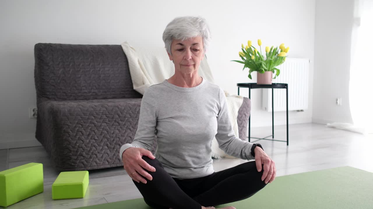 白发苍苍的活跃老年妇女在家里的瑜伽垫上做颈部伸展运动视频素材