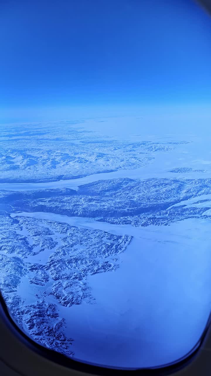 从蓝色的飞机窗户向外俯瞰下面的雪山视频素材