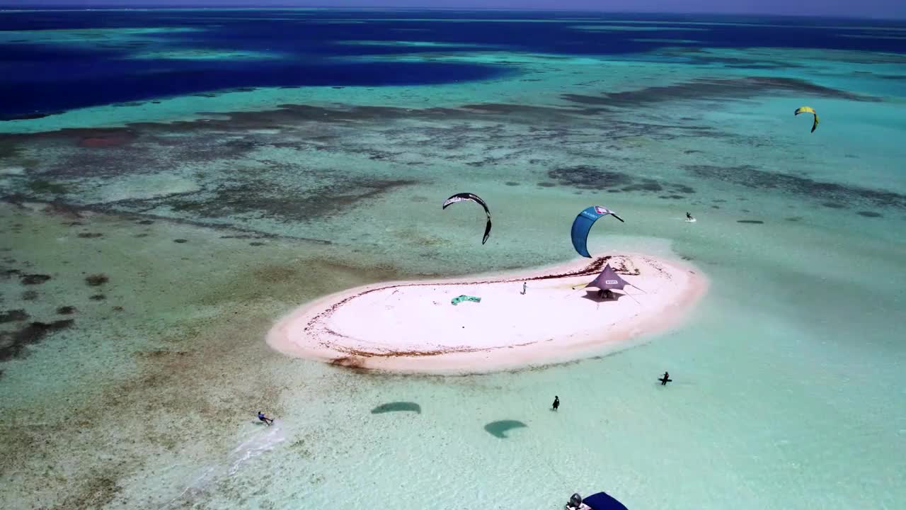 风筝冲浪周围的一个小，孤立的沙岛在清澈的蓝色海水，鸟瞰图视频素材