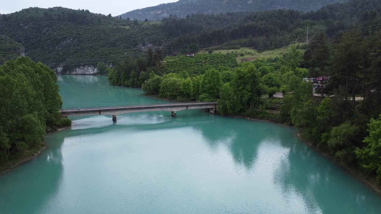 无人机俯瞰绿松石山湖和横跨湖面的桥梁。翡翠湖坐落在岩石地形和茂密的森林中。桥跨湖，展现宁静的湖、桥和周围的自然视频素材