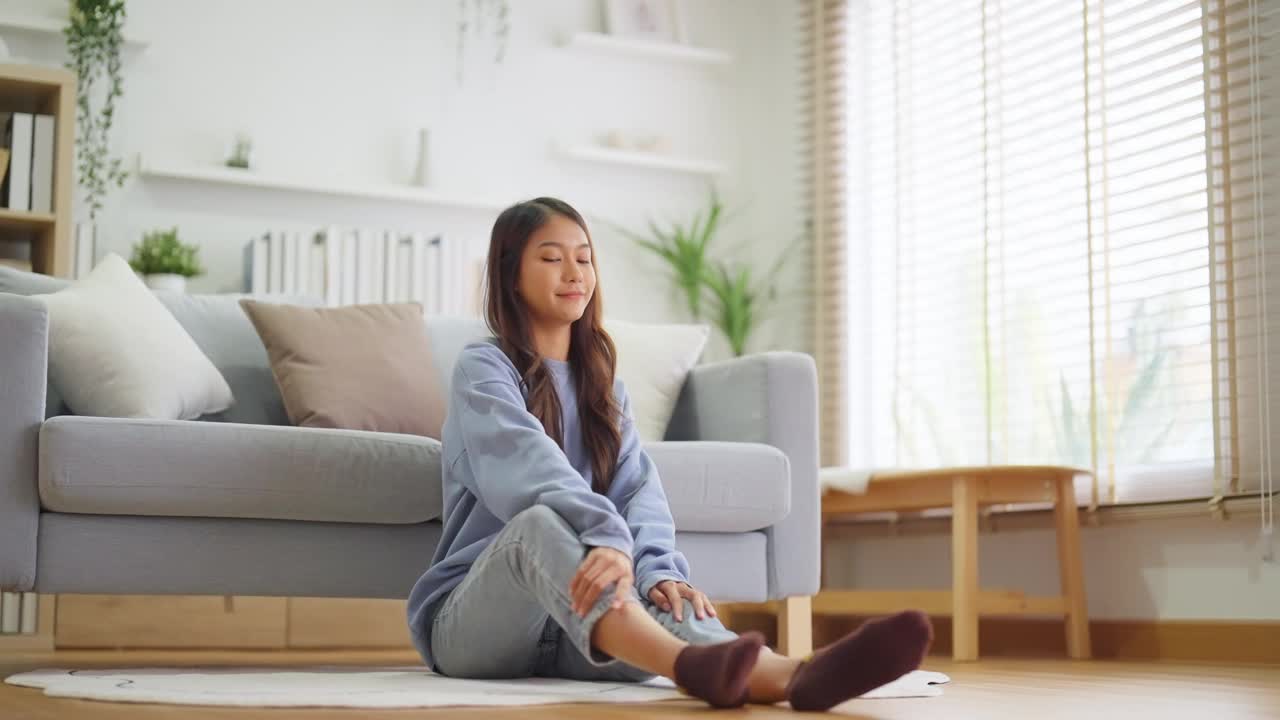 快乐的年轻亚洲女性在家里练习瑜伽和冥想，坐在客厅的地板上，以莲花的姿势，闭上眼睛放松。正念冥想和幸福概念视频素材