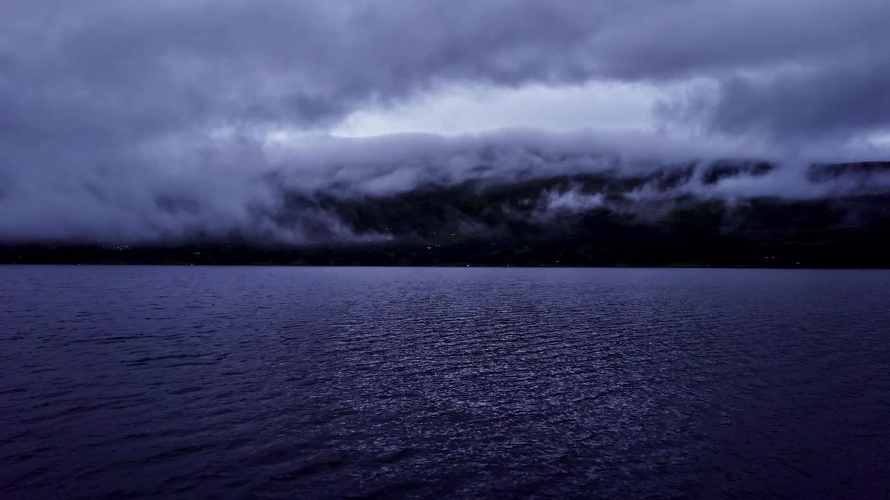 在挪威峡湾的夜晚，无人机在波光粼粼的湖面上向后低空飞行视频素材