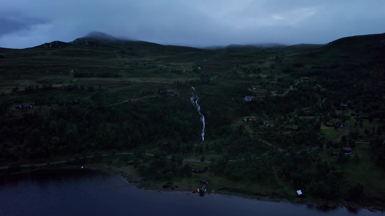 空中黄昏轨道拍摄的小屋和流动的溪流在山腰与低云在山脊视频素材