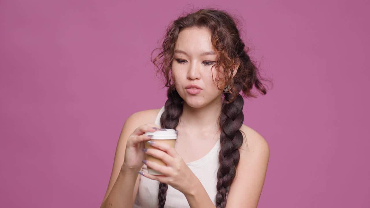 年轻女子小心翼翼地打开咖啡杯盖，背景是充满活力的粉红色视频素材