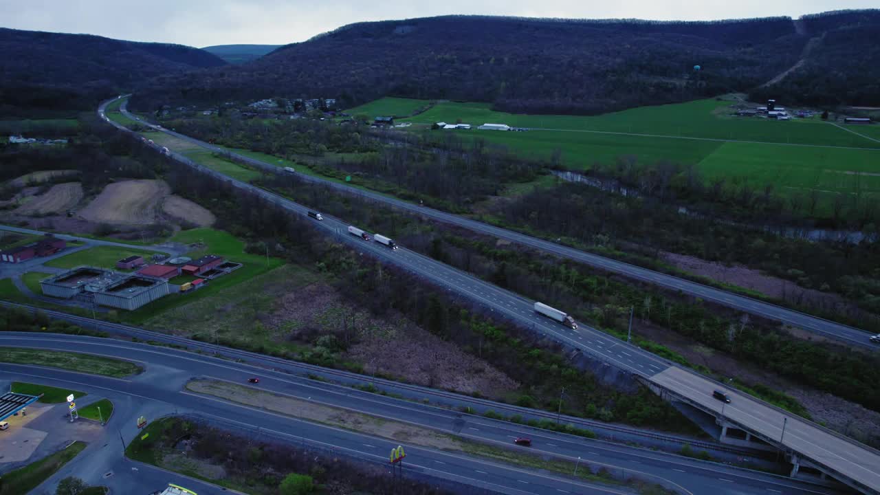 高架拍摄的半卡车行驶在80号州际公路上，周围环绕着茂密的绿色植物和山丘。美国视频素材