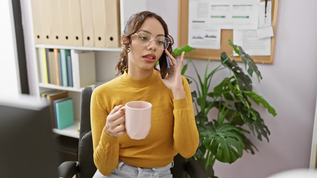 在现代化的办公室里，穿着黄色衣服的女人拿着杯子在讲电话视频素材