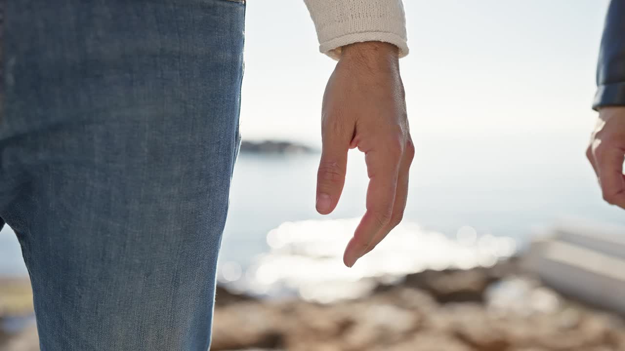 一个男人和一个女人在海边牵手，在大海的背景下象征着爱和团聚。视频素材