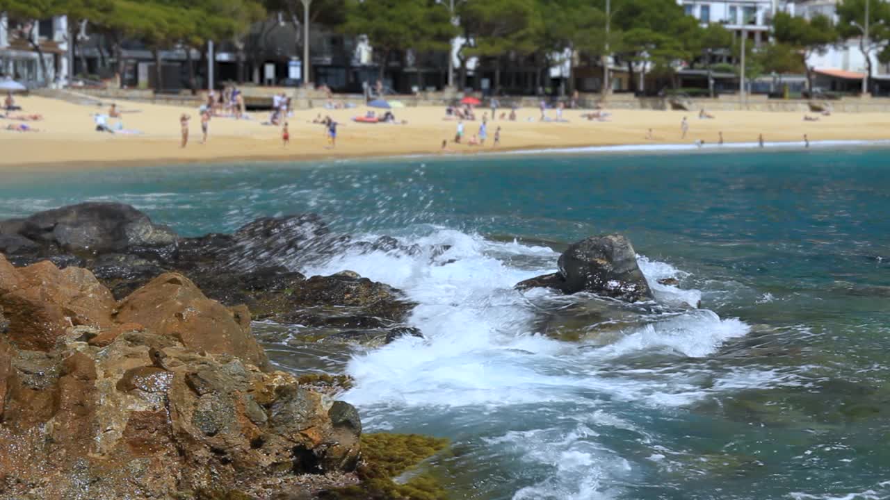 海浪拍打着岩石。背景是在拉弗朗克海滩上游泳的人。布拉瓦海岸，加泰罗尼亚，西班牙视频素材