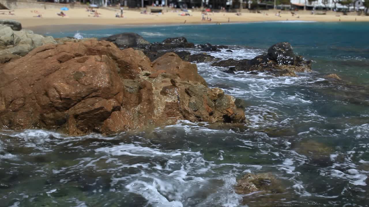 地中海的海水冲刷着海湾周围的岩石。背景是拉弗朗克海滩。布拉瓦海岸，加泰罗尼亚，西班牙。视频素材