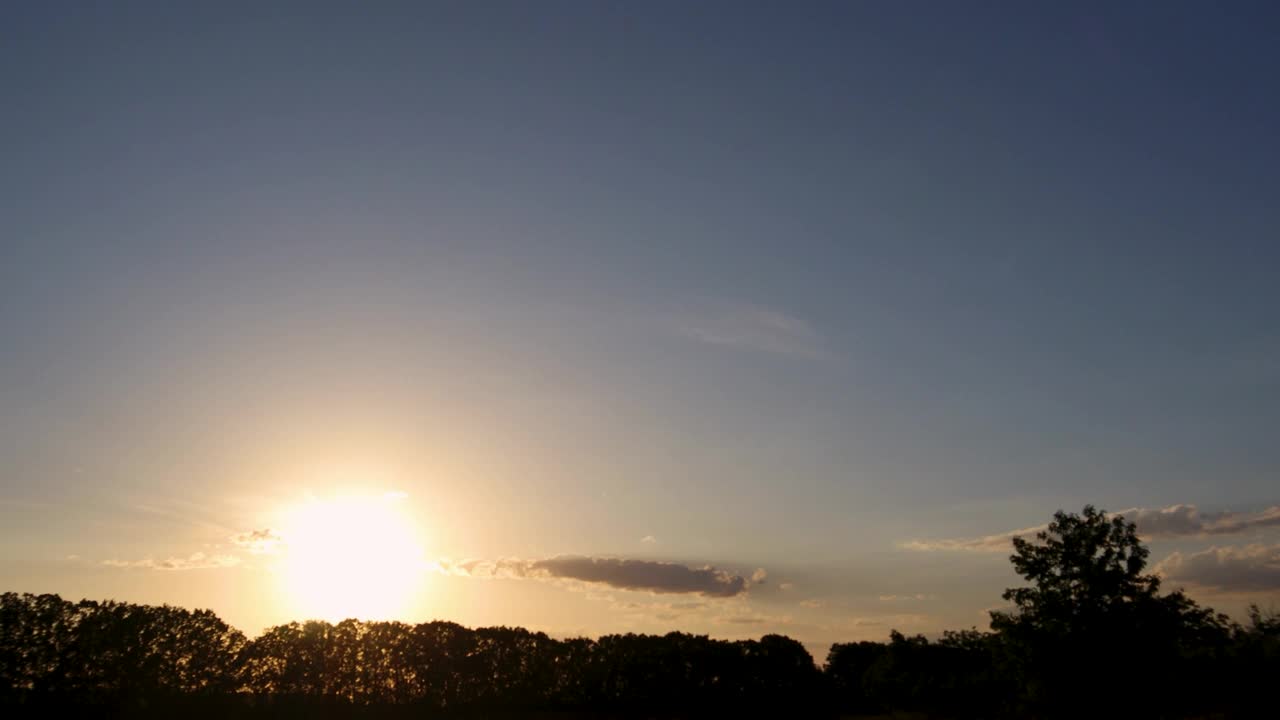 明亮的阳光穿过树木的剪影，在宁静的日落场景中映衬着充满活力的天空视频素材