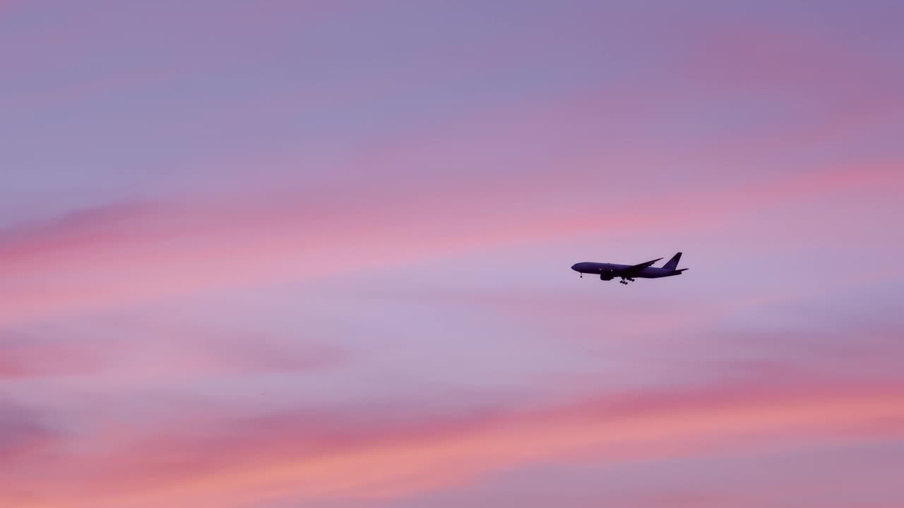 飞机在天空中飞行，在粉红色和橙色的日出或日落。大飞机在夕阳下的天空。旅游和交通的概念。视频下载