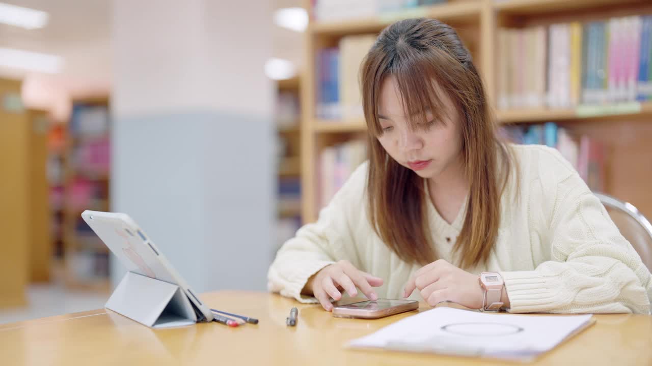 一个女人坐在桌子旁，面前放着一台平板电脑和一部手机视频素材