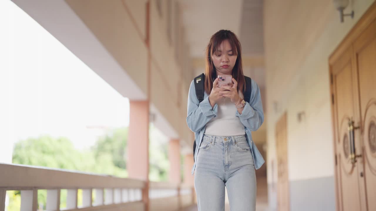 一个年轻女子手里拿着手机走在走廊上视频素材