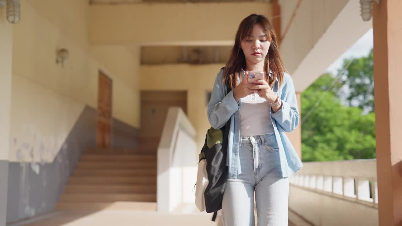 一个年轻女子手里拿着手机走在走廊上视频素材