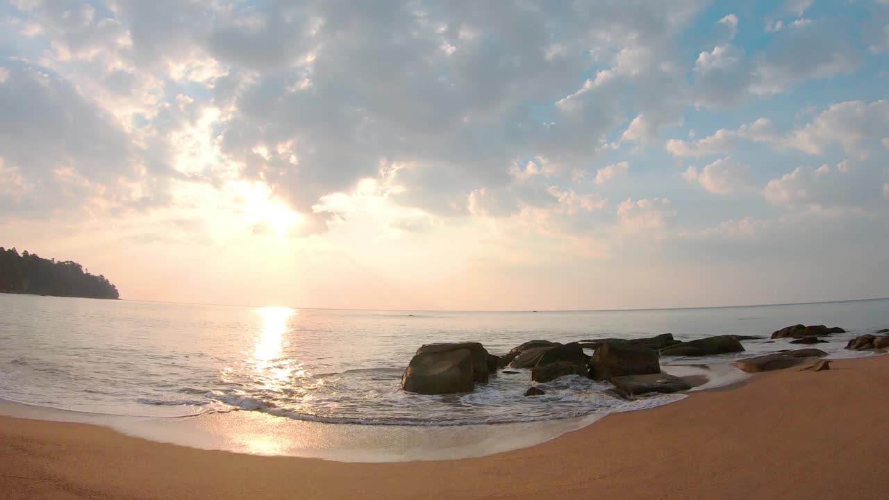 广角海景沙滩日落。柔和的天空云移动到太阳下的海水在水平。沙滩上的黑岩。自然背景和夏季目的地景观4k延时镜头视频素材