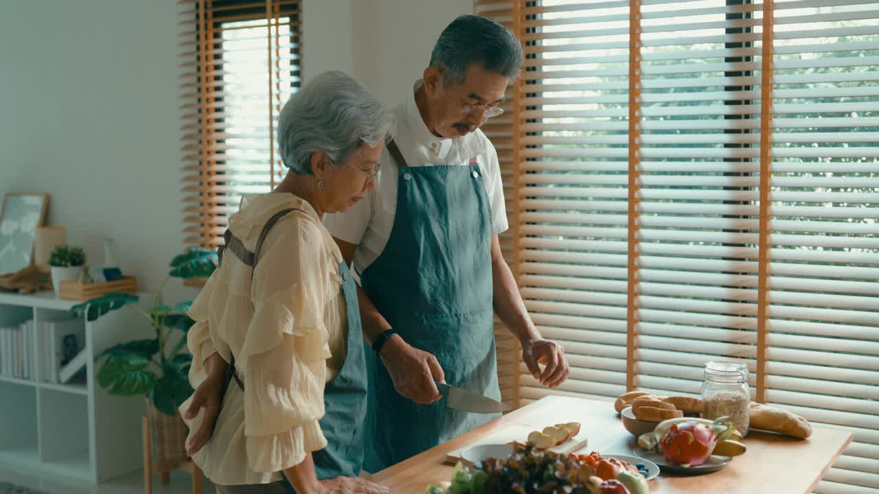 一对亚洲老年夫妇正在准备一顿健康餐，在家里为沙拉切水果和蔬菜。可持续的生活。视频素材