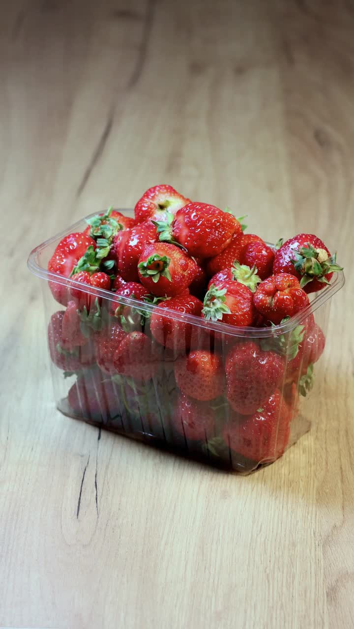 垂直视图的农民谁正在拿一个新鲜的红色草莓包装在木制背景。视频下载