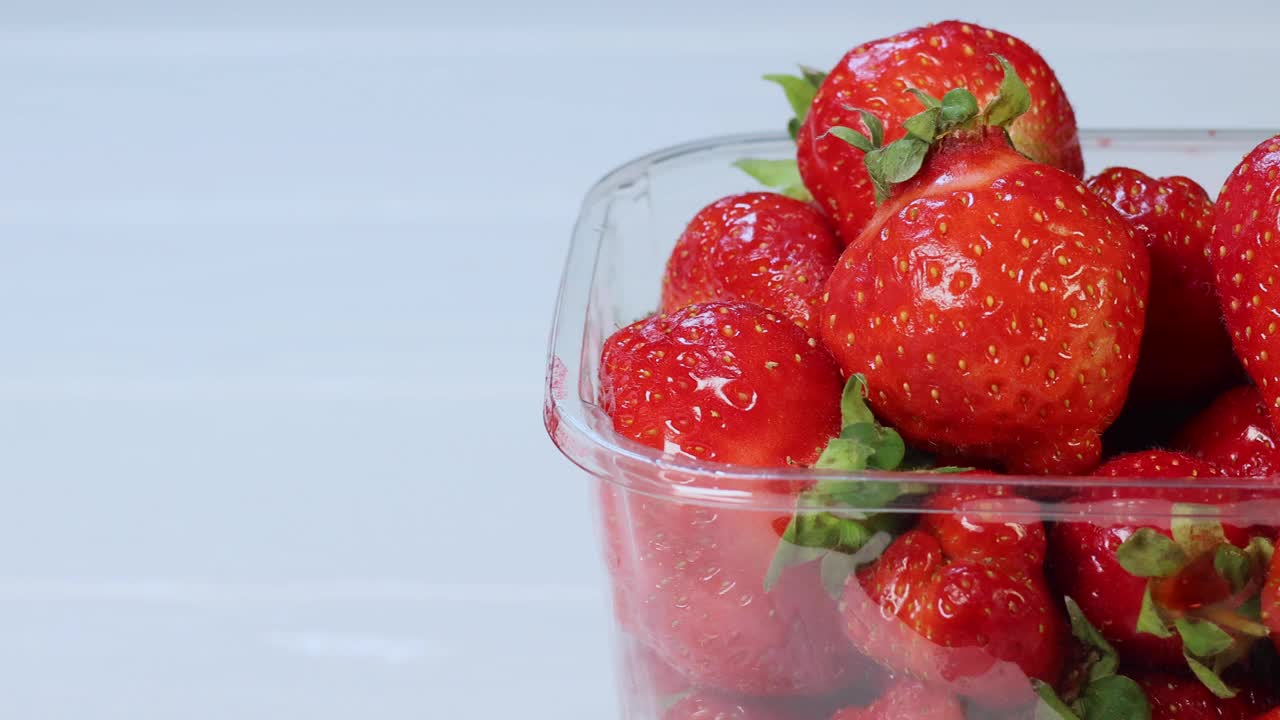 新鲜的红草莓装在白色木制背景的包装里。视频下载