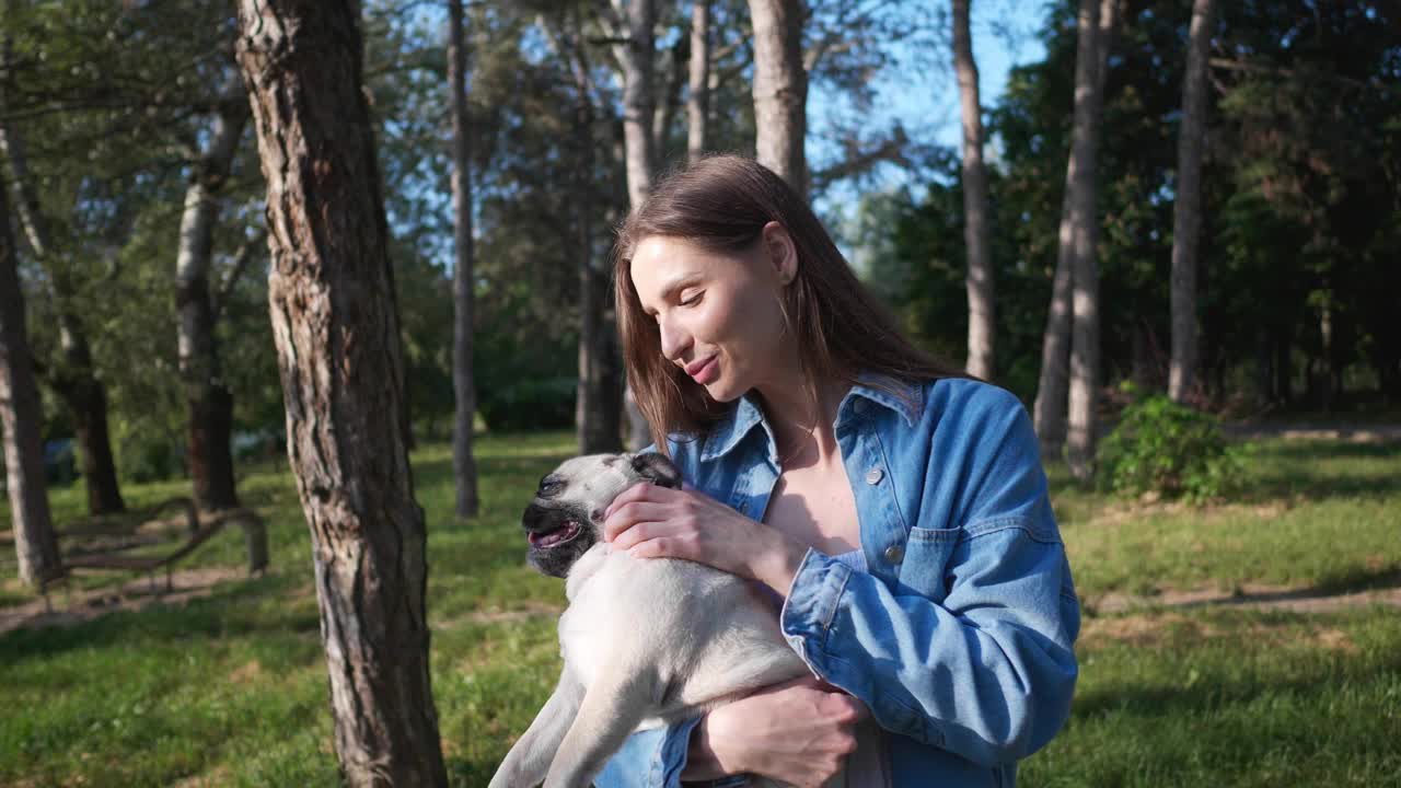 阳光明媚的早晨，快乐的年轻女子和她可爱的哈巴狗在公园里。镜头移动，慢动作效果视频素材