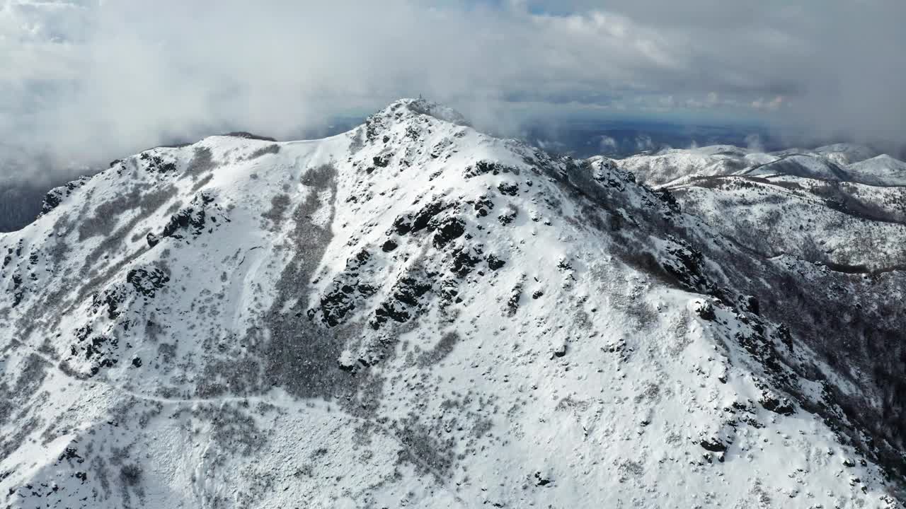 多云的天空下白雪皑皑的山峰，鸟瞰图捕捉到崎岖的地形和广阔的荒野视频素材