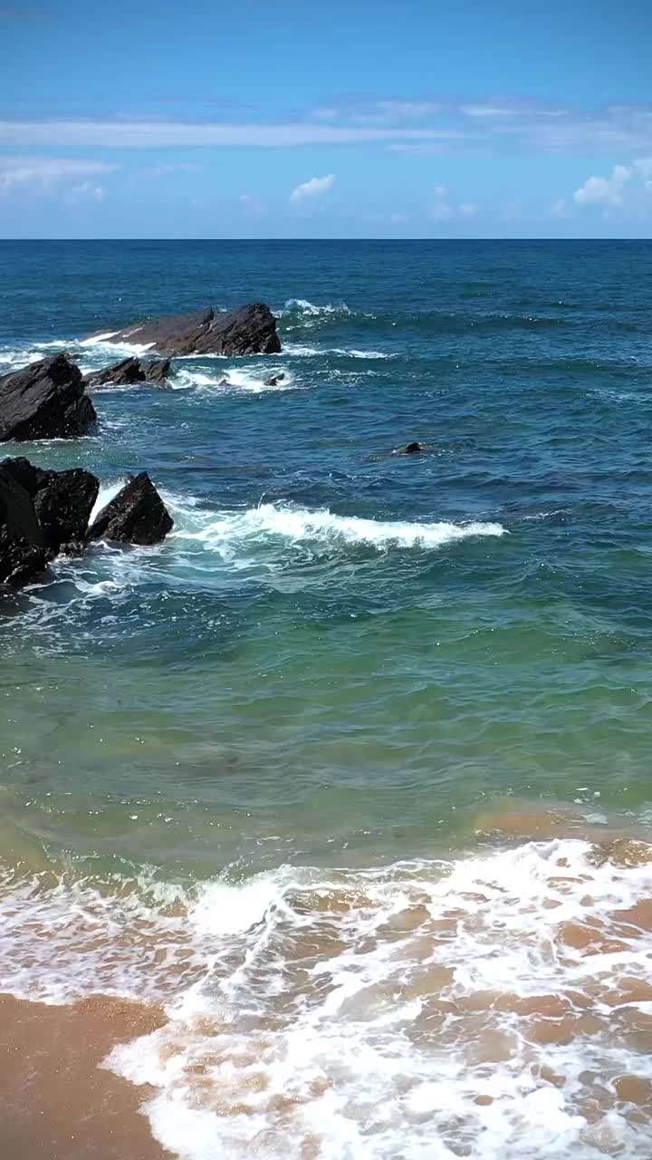 海浪，沙子和岩石在海滩上，岩石在水里视频下载