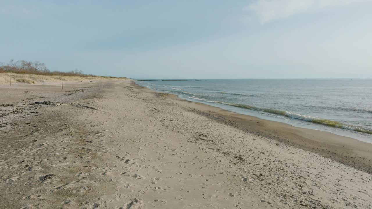 在一个阳光明媚的春日，拉脱维亚的波罗的海，佩普海滩，海浪冲击着白色沙滩的航拍视图，上升的广角无人机镜头向前移动视频素材