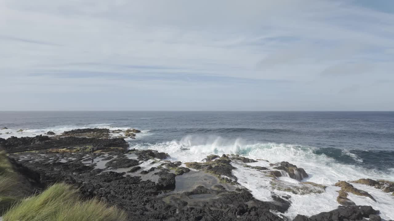 在圣米格尔的莫斯泰罗斯，海浪冲击着岩石海岸，天空晴朗，远处有悬崖视频素材