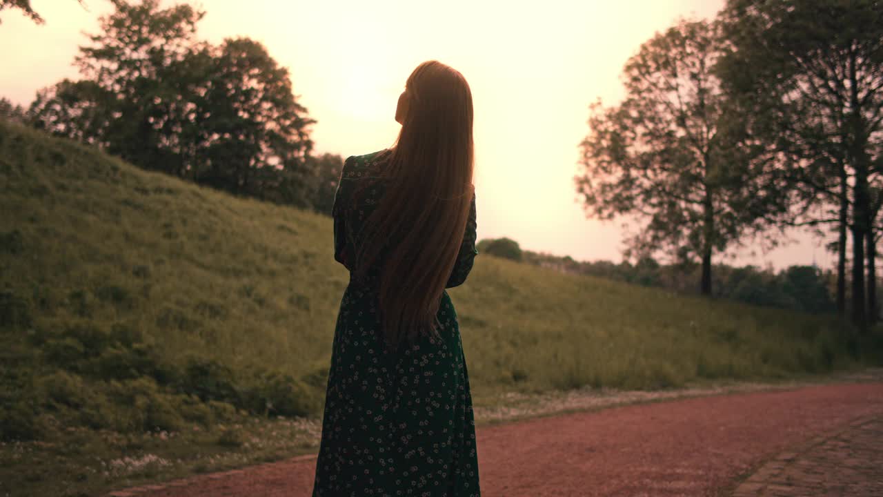 年轻美丽的女人在夏日的大自然中穿着绿色的长裙散步。视频素材