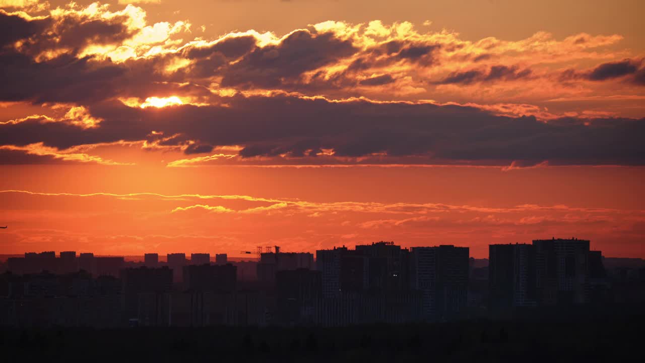 黄昏的城市天际线上，高高的屋顶，随着时间的流逝，夕阳在云层上投下红光。视频下载