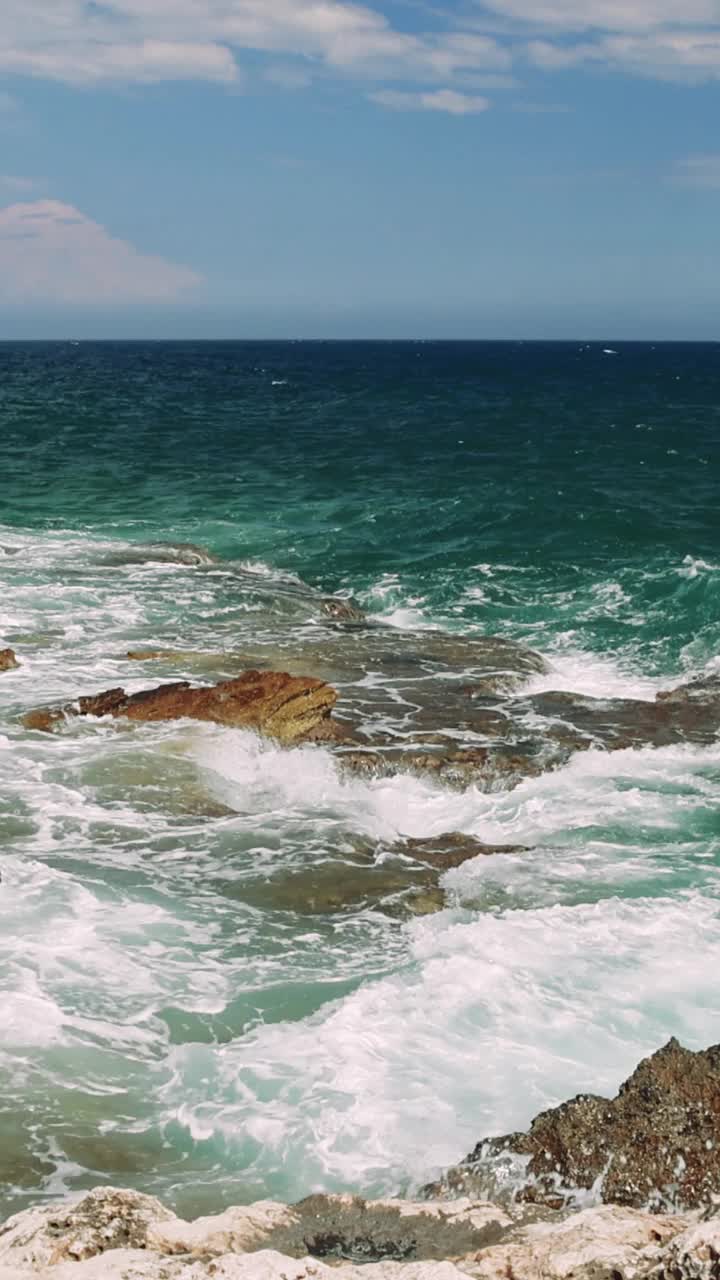 雄伟的舞蹈:一瞥从岩石悬崖绿松石海洋体验强大的海浪的绿松石海洋撞击崎岖的岩石从一个惊人的观点在悬崖上。视频素材